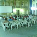 MovieMovil, la empresa de cine al aire libre, convierte el Ayuntamiento de Elda en un escenario cinematográfico único Proyección de cine al aire libre frente al Ayuntamiento de Elda, con una gran pantalla blanca instalada en la fachada del edificio. Filas de sillas blancas están dispuestas para el público, que disfruta de la película en un ambiente nocturno y comunitario. MovieMovil, la empresa de cine al aire libre