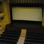 MovieMovil, la empresa de cine al aire libre, transforma el Teatro Principal de Banyeres de Mariola en un espacio cinematográfico único Interior del Teatro Principal de Banyeres de Mariola, con una gran pantalla blanca situada en el escenario, rodeada de altavoces y filas de asientos dispuestas en niveles. El espacio está vacío, destacando la arquitectura clásica del teatro. MovieMovil, la empresa de cine al aire libre