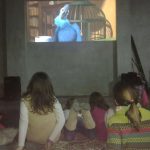 MovieMovil, la empresa de cine al aire libre, lleva la magia del cine a fiestas infantiles en espacios privados Proyección de cine en un local privado durante una fiesta infantil, con niños sentados en el suelo viendo una película animada protagonizada por un pájaro azul, mientras un perro pequeño descansa junto a ellos. MovieMovil, la empresa de cine al aire libre