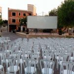 MovieMovil, la empresa de cine al aire libre, ofrece una experiencia única sobre el río en Rojales Proyección de cine al aire libre en El Malecón del Soto en Rojales (Alicante), justo sobre el río, con una pantalla grande, sillas blancas para el público y árboles en el fondo. MovieMovil, la empresa de cine al aire libre