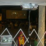 MovieMovil, la empresa de cine al aire libre, combina historia y entretenimiento en Beneixama Proyección de cine al aire libre en Beneixama junto a la pared de su castillo, con una pantalla grande mostrando una película, público sentado en sillas blancas y equipo técnico gestionando la proyección. MovieMovil, la empresa de cine al aire libre