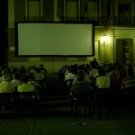 MovieMovil, la empresa de cine al aire libre, convierte el Ayuntamiento de Elda en un escenario cinematográfico único Proyección de cine al aire libre frente al Ayuntamiento de Elda, con una gran pantalla montada en la fachada del edificio. Filas de sillas están dispuestas para el público, que disfruta de la película en un ambiente nocturno iluminado por las luces del edificio y farolas cercanas. MovieMovil, la empresa de cine al aire libre
