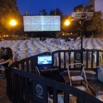 MovieMovil, la empresa de cine al aire libre, organiza espectáculos únicos bajo las estrellas Proyección de cine al aire libre con pantalla grande mostrando ruido visual estático, mientras el público, sentado en sillas blancas, disfruta de la experiencia. MovieMovil, la empresa de cine al aire libre