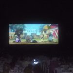 MovieMovil, la empresa de cine al aire libre, ofrece momentos inolvidables con películas animadas Pantalla de cine al aire libre proyectando una película animada mientras el público, sentado en sillas de plástico blanco, disfruta de la experiencia. MovieMovil, la empresa de cine al aire libre