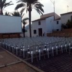 MovieMovil la empresa del cine al aire libre transforma Altea en un escenario mágico para disfrutar del cine bajo las estrellas. Cine al aire libre en Altea, organizado por MovieMovil la empresa del cine al aire libre, con pantalla gigante, sillas blancas y un entorno pintoresco con palmeras y edificios tradicionales.
