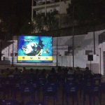 MovieMovil la empresa del cine al aire libre conecta a la comunidad con proyecciones mágicas al aire libre en escenarios únicos. Proyección al aire libre organizada por MovieMovil la empresa del cine al aire libre. El público está sentado en filas de sillas patrocinadas por Pepsi, y el entorno incluye estructuras arquitectónicas en el fondo.