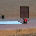 MovieMovil, la empresa de cine al aire libre, transforma Ibi en un escenario cinematográfico único Montaje de una pantalla de cine al aire libre en Ibi, con una persona en una plataforma de ladrillo ajustando una gran pantalla blanca. El escenario tiene una pared frontal con graffiti, y al fondo se observa una puerta grande de ladrillo. MovieMovil, la empresa de cine al aire libre