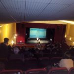 MovieMovil, la empresa de cine al aire libre, participa en congresos benéficos con proyecciones impactantes Texto alternativo: Proyección en un auditorio cerrado durante un congreso benéfico, con una pantalla grande mostrando el mensaje "Razones para vivir", público sentado en sillas rojas y equipo técnico en el escenario. MovieMovil, la empresa de cine al aire libre