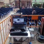 MovieMovil la empresa del cine al aire libre transforma la Plaza de la Iglesia de El Campello en un escenario mágico para disfrutar del cine bajo las estrellas. Proyección de cine al aire libre en la Plaza de la Iglesia de El Campello, organizada por MovieMovil la empresa del cine al aire libre. El público está sentado en filas de sillas azules, con un proyector y equipo de audio cuidadosamente instalados en el centro del evento.